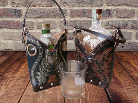 Two cowboy boot-shaped liquor holders with bottles inside on a wooden surface against a brick wall.