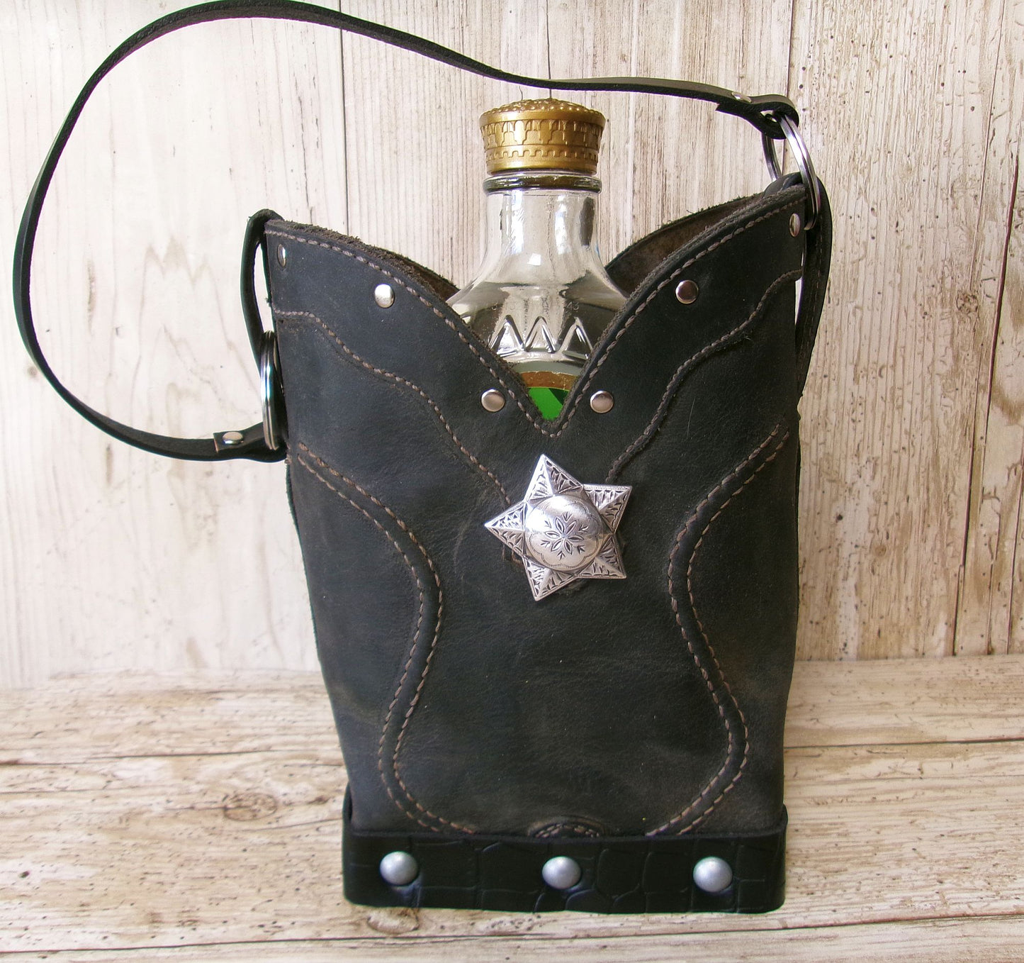 Black leather flask holder with star accent containing a bottle on a wooden surface