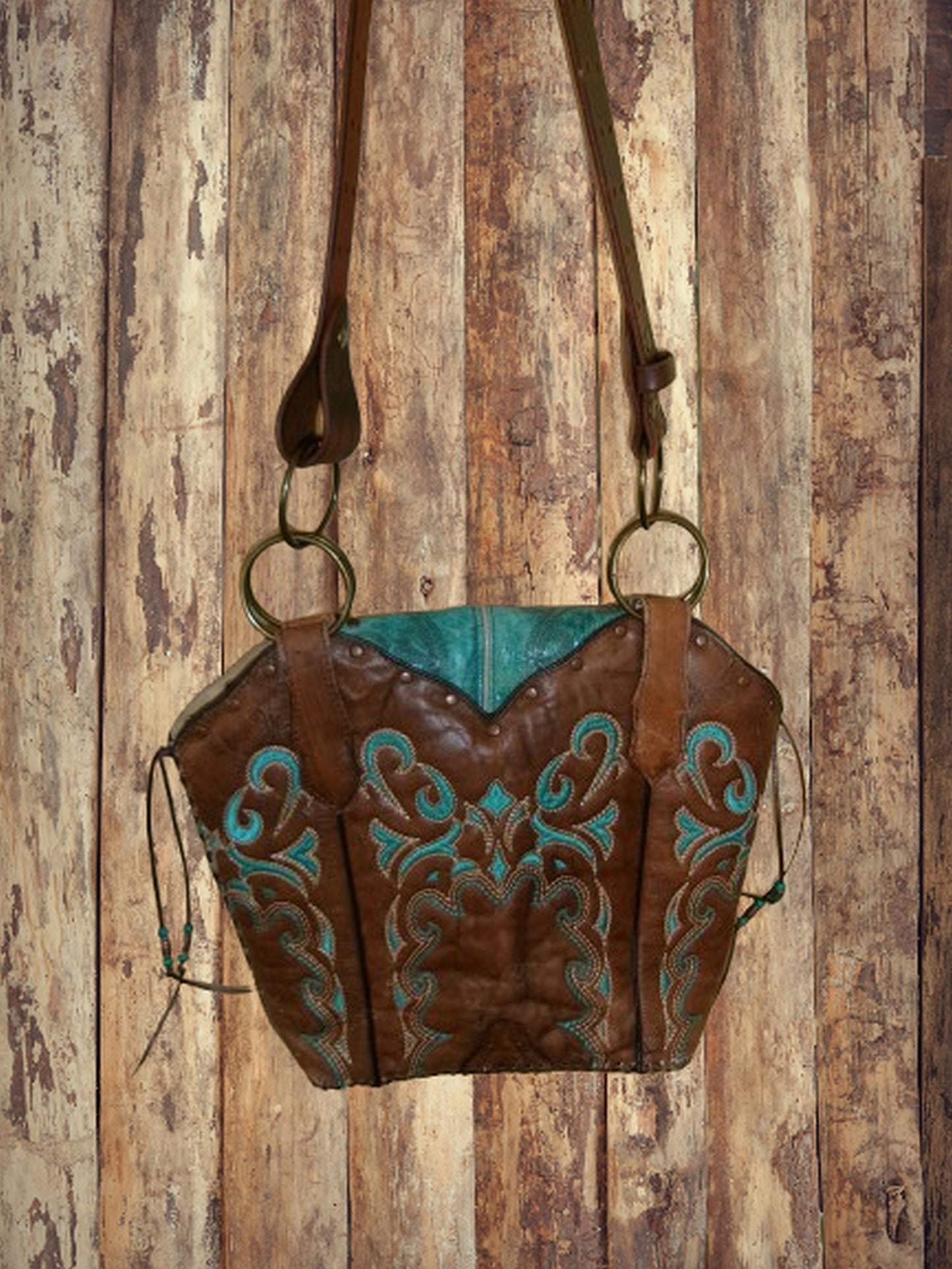 Brown leather handbag with turquoise designs on a wooden background