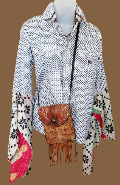 Mannequin wearing a patterned shirt with colorful sleeves, holding a brown leather bag with fringes on a brown background.