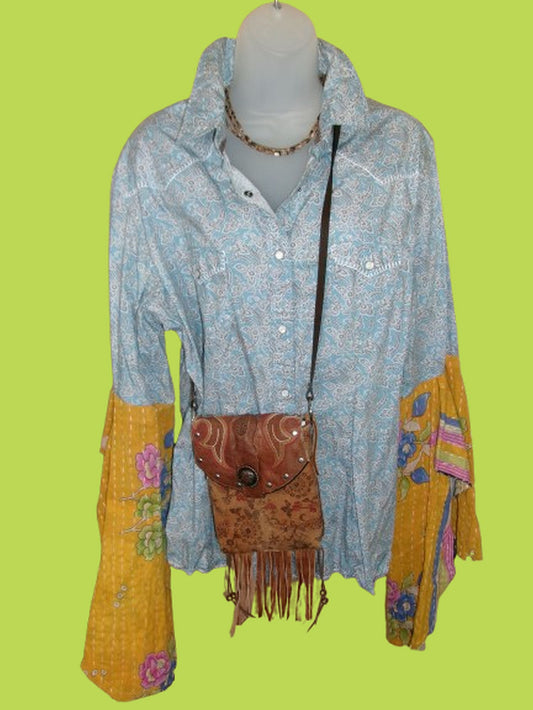 Mannequin wearing a blue floral shirt with yellow accents and a brown fringed bag on a green background