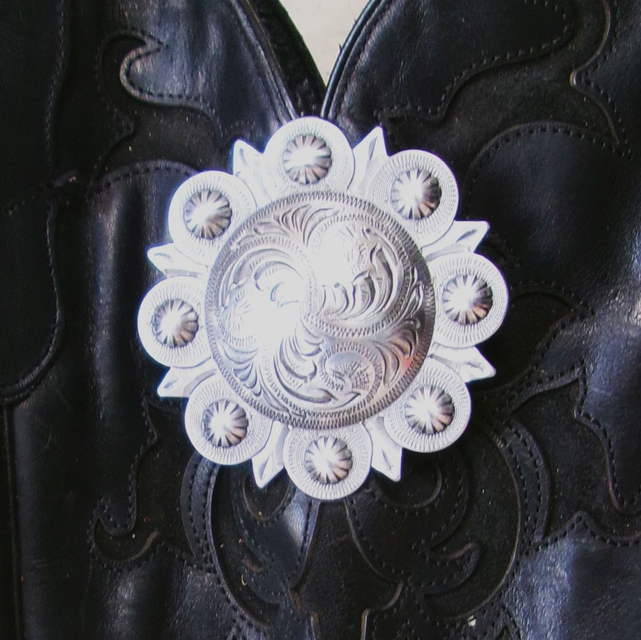 Decorative silver concho on a black leather background