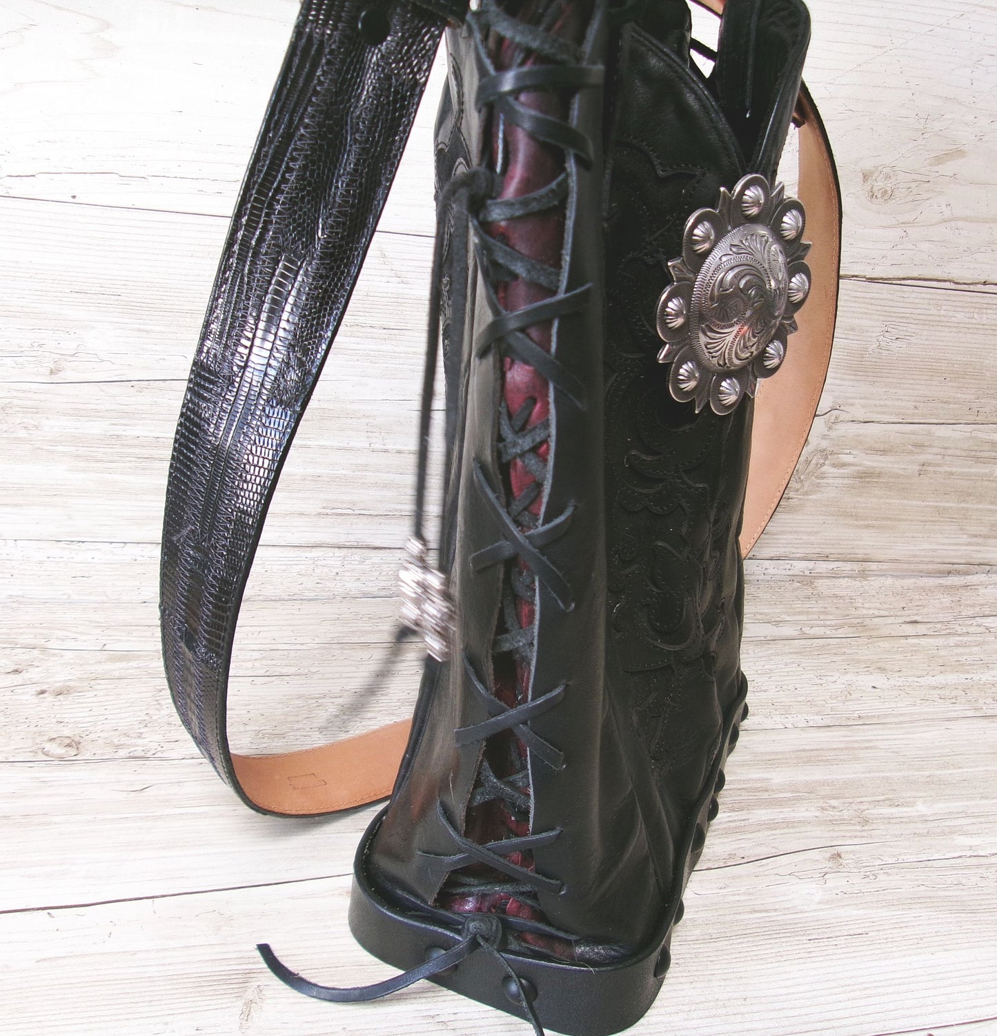Black lace-up boots with decorative concho on a wooden floor