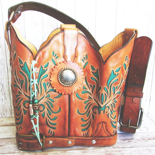 Brown leather handbag with intricate green and turquoise designs on a wooden surface.