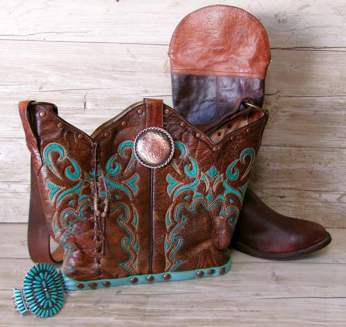 Brown leather boot with turquoise embroidery and decorative elements on a wooden surface.