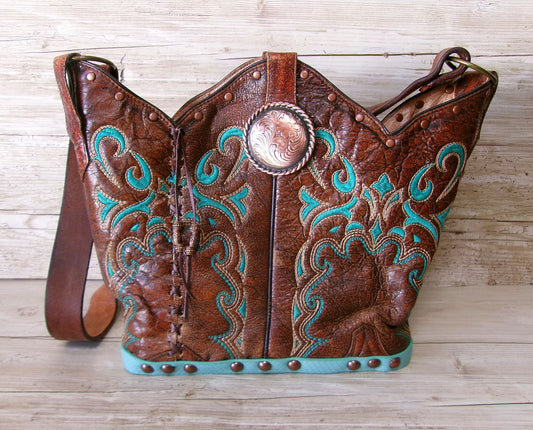 Brown leather handbag with turquoise embroidery and decorative studs on a wooden surface