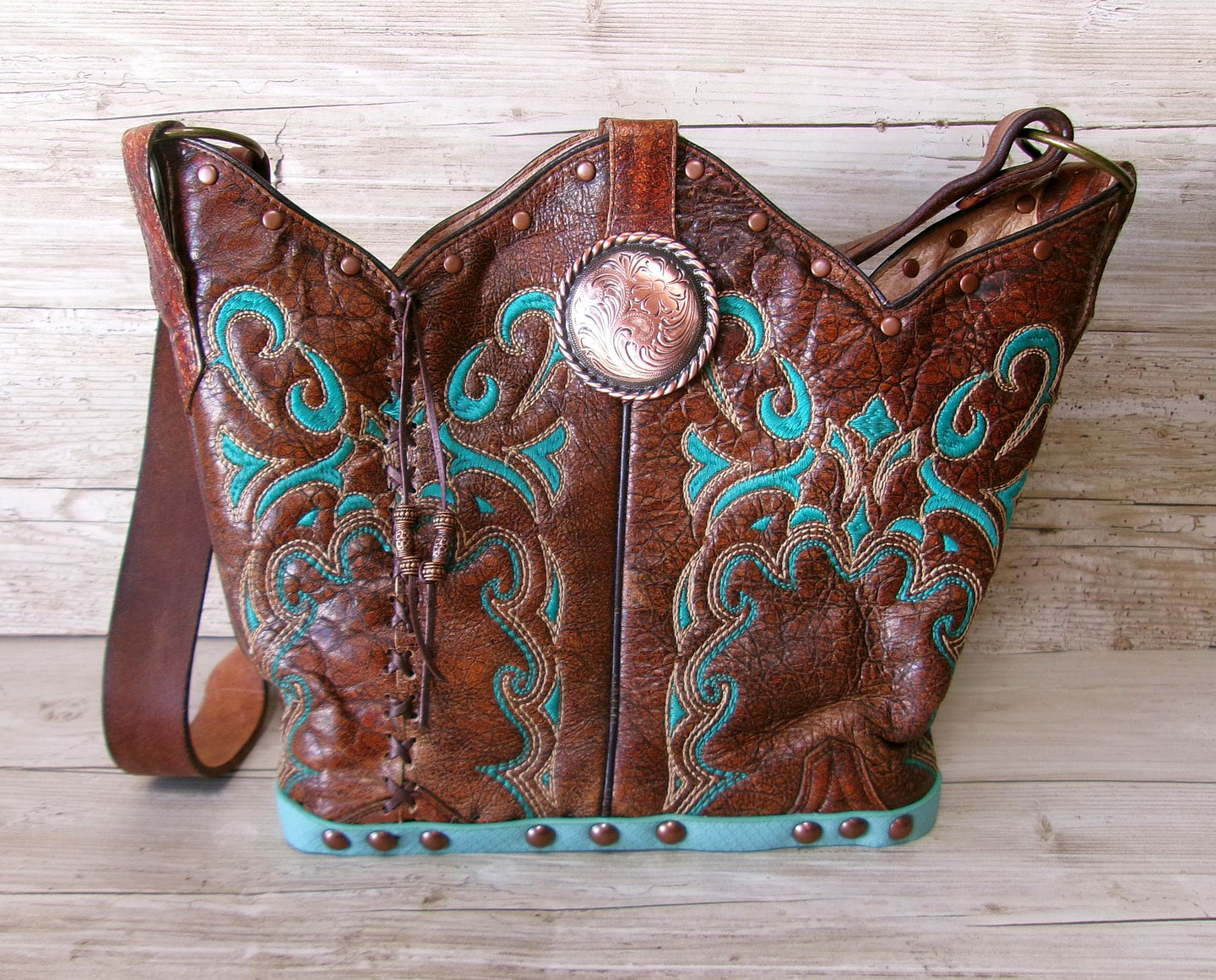 Brown leather handbag with turquoise embroidery and decorative studs on a wooden surface