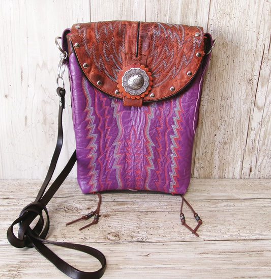 Purple patterned bag with brown leather flap on a wooden surface