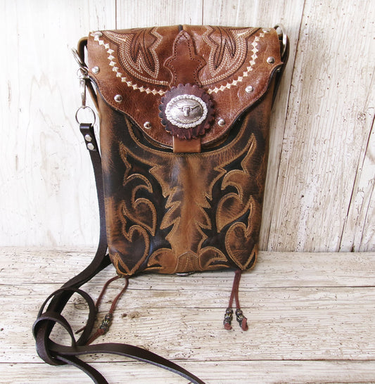 Brown leather bag with intricate patterns and a concho on a wooden surface