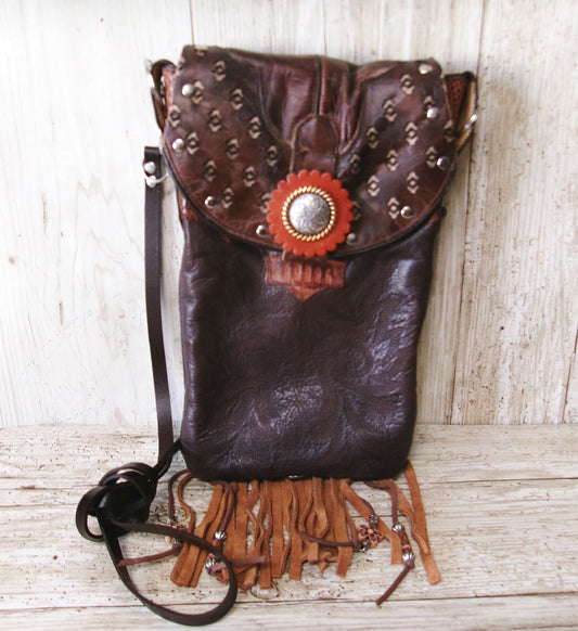Brown leather bag with studs and a red flower on a wooden surface