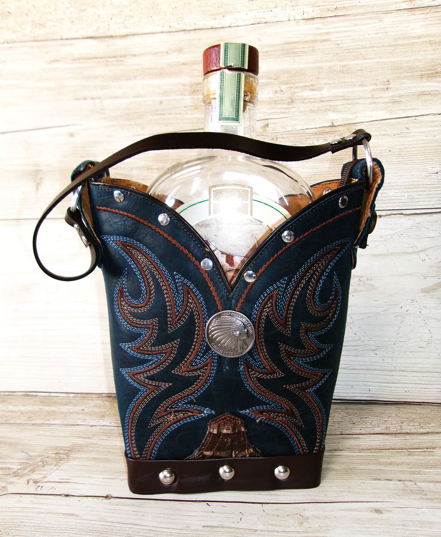 Clear glass bottle with decorative blue leather holder on a wooden surface