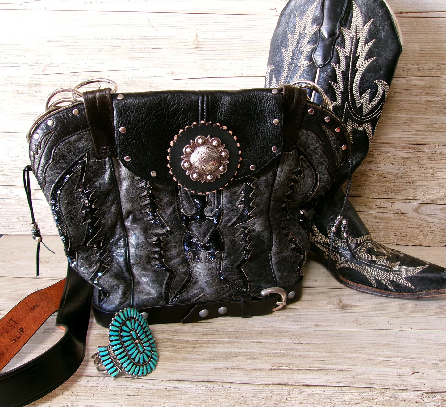 Black leather handbag with cowboy boot design and turquoise earrings on a wooden surface