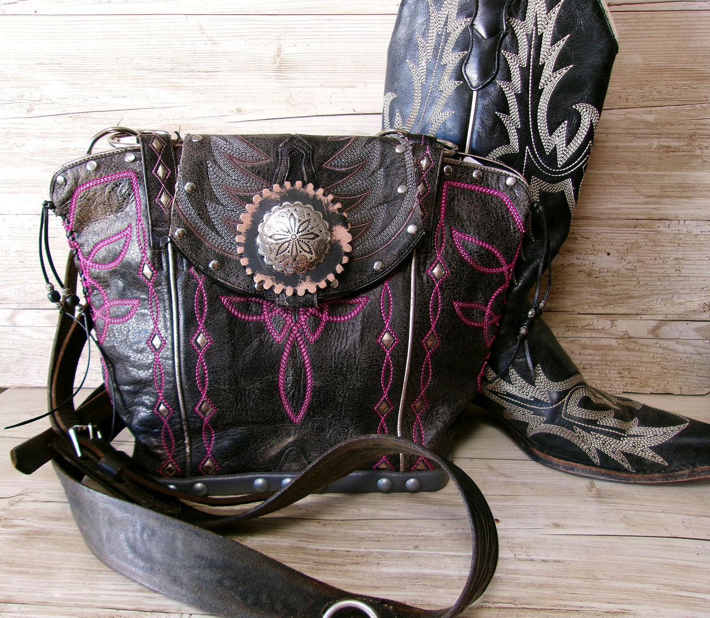 Decorative leather bag with pink embroidery and a matching boot on a wooden surface