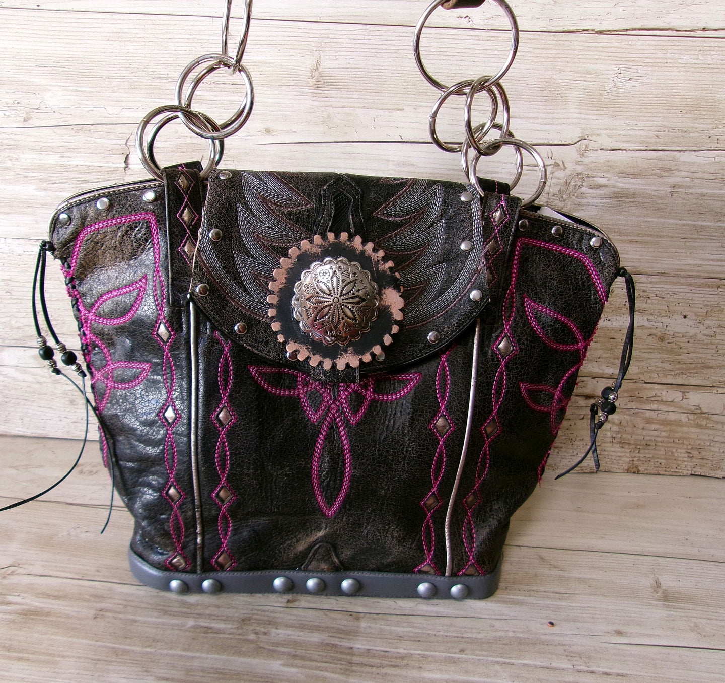 Black leather handbag with pink embroidery and decorative studs on a wooden surface