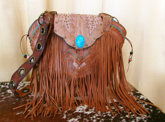 Brown leather handbag with fringe and decorative elements on a wooden surface.