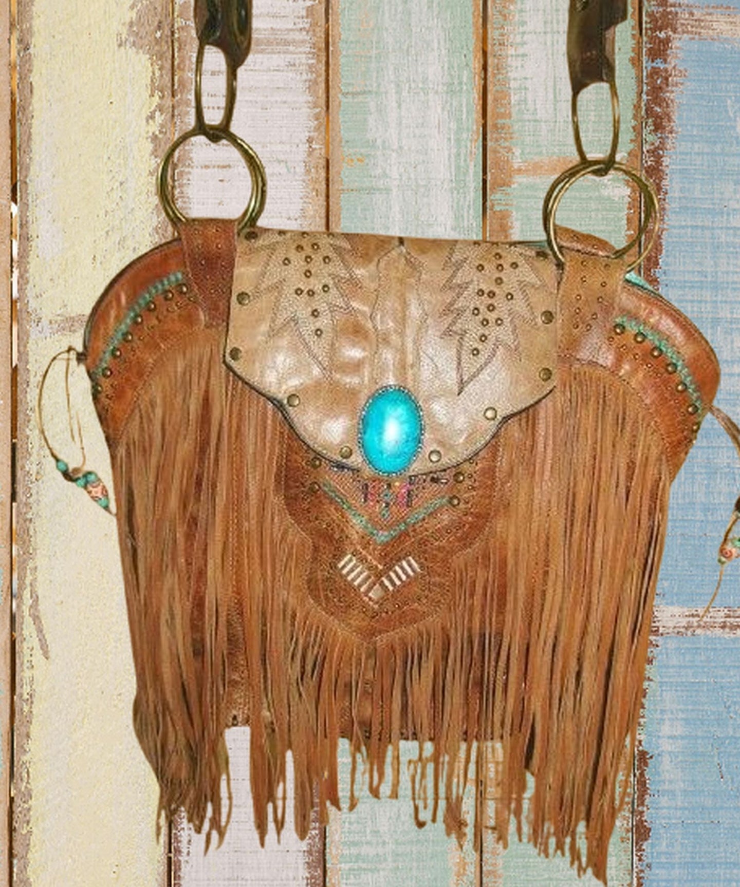 Brown leather handbag with fringe and turquoise stone on a textured background