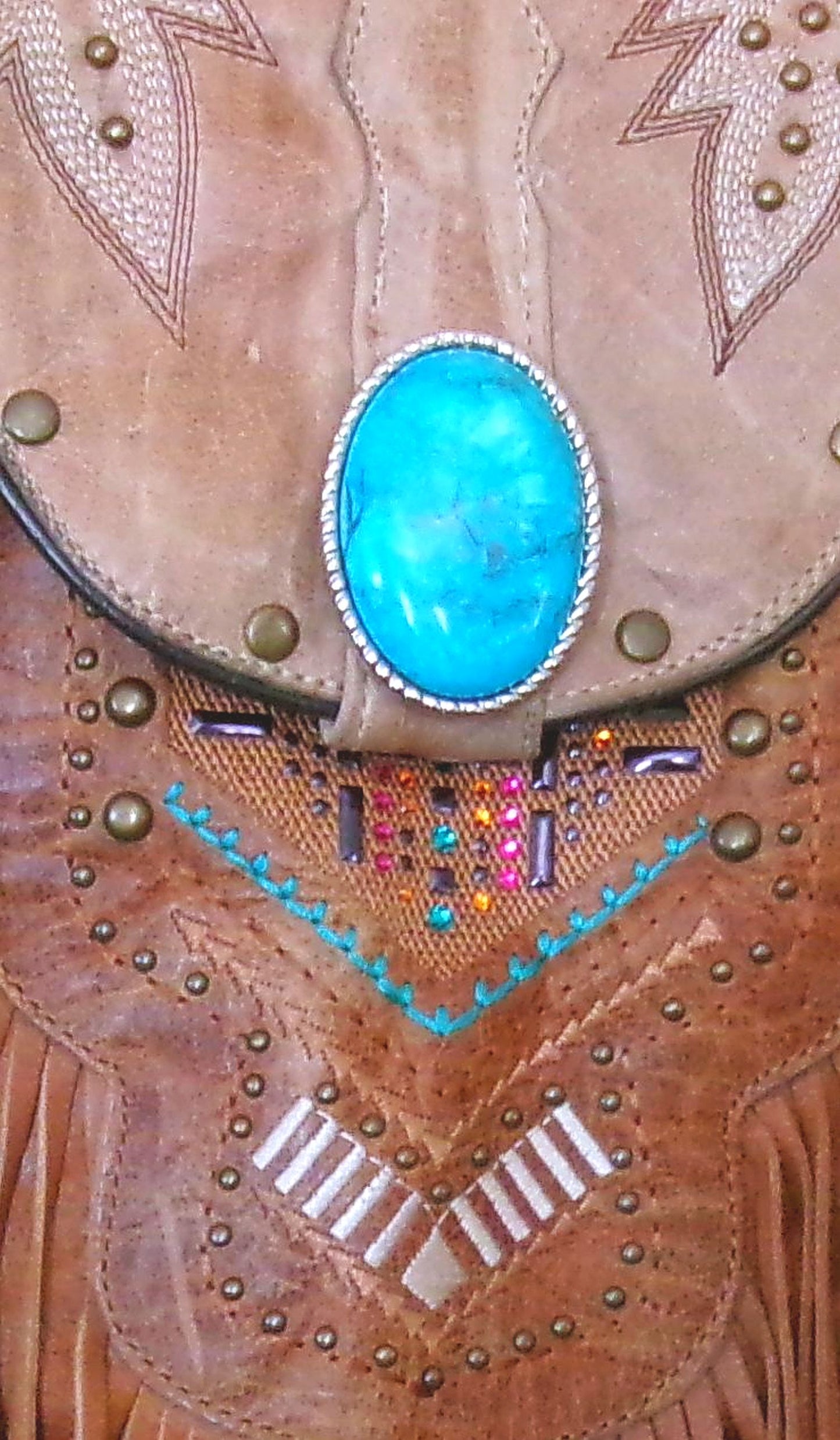 Close-up of a decorative leather item with turquoise stone and fringe details