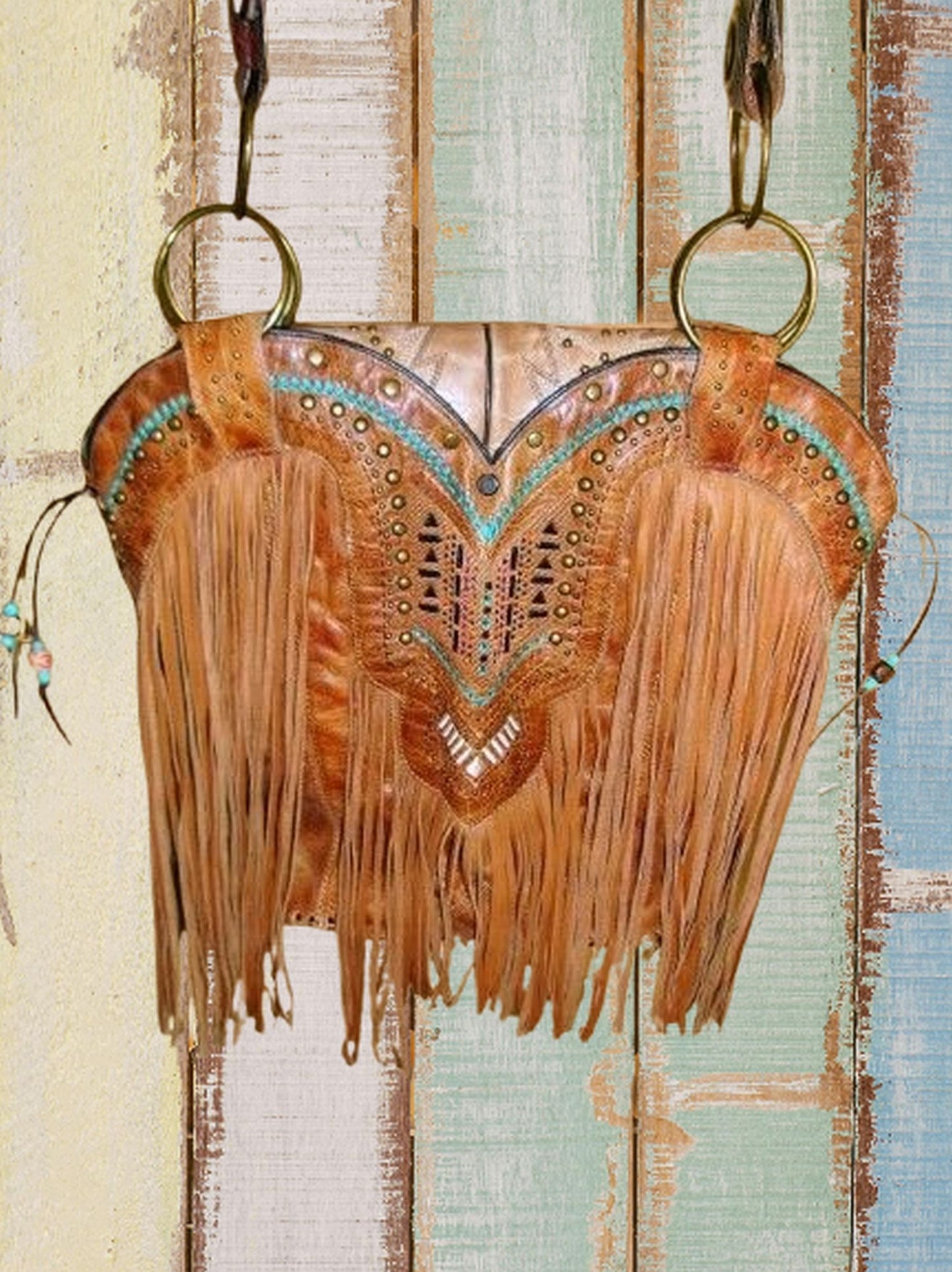 Decorative leather bag with fringe and intricate patterns on a textured wooden background