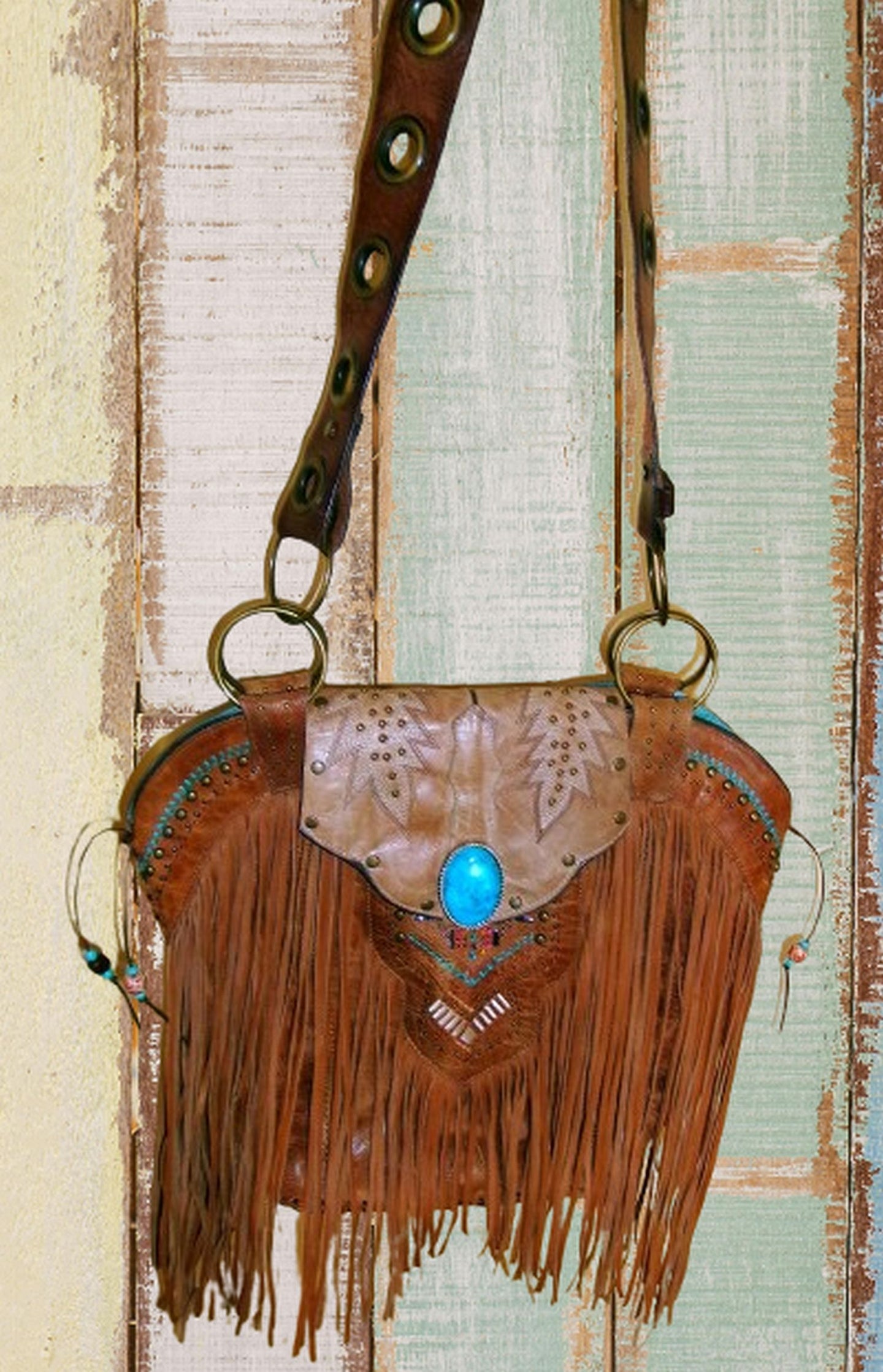 Brown leather crossbody bag with fringe and blue stone on a rustic wooden background
