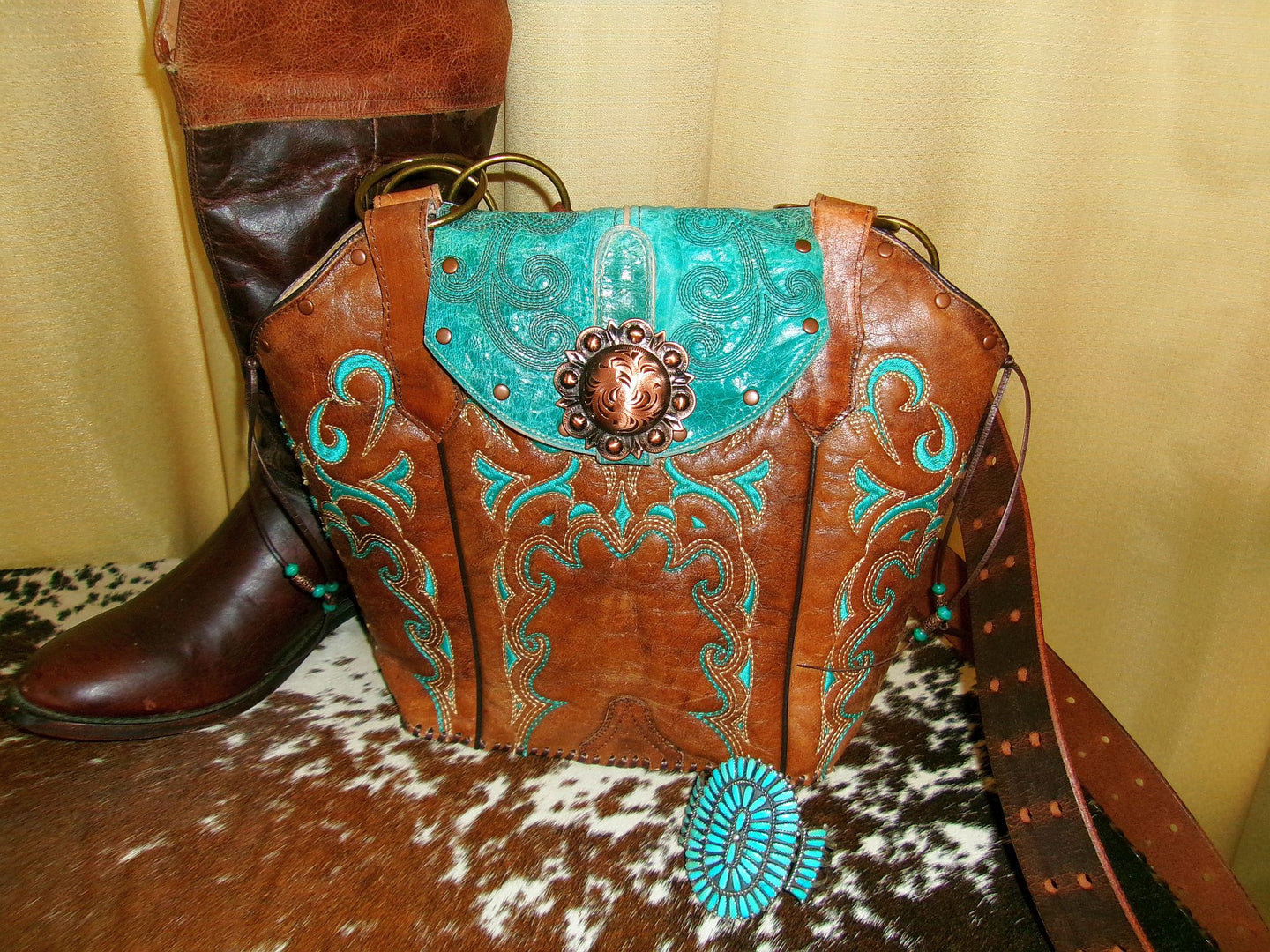 Brown leather bag with turquoise accents and decorative elements on a cowhide surface.