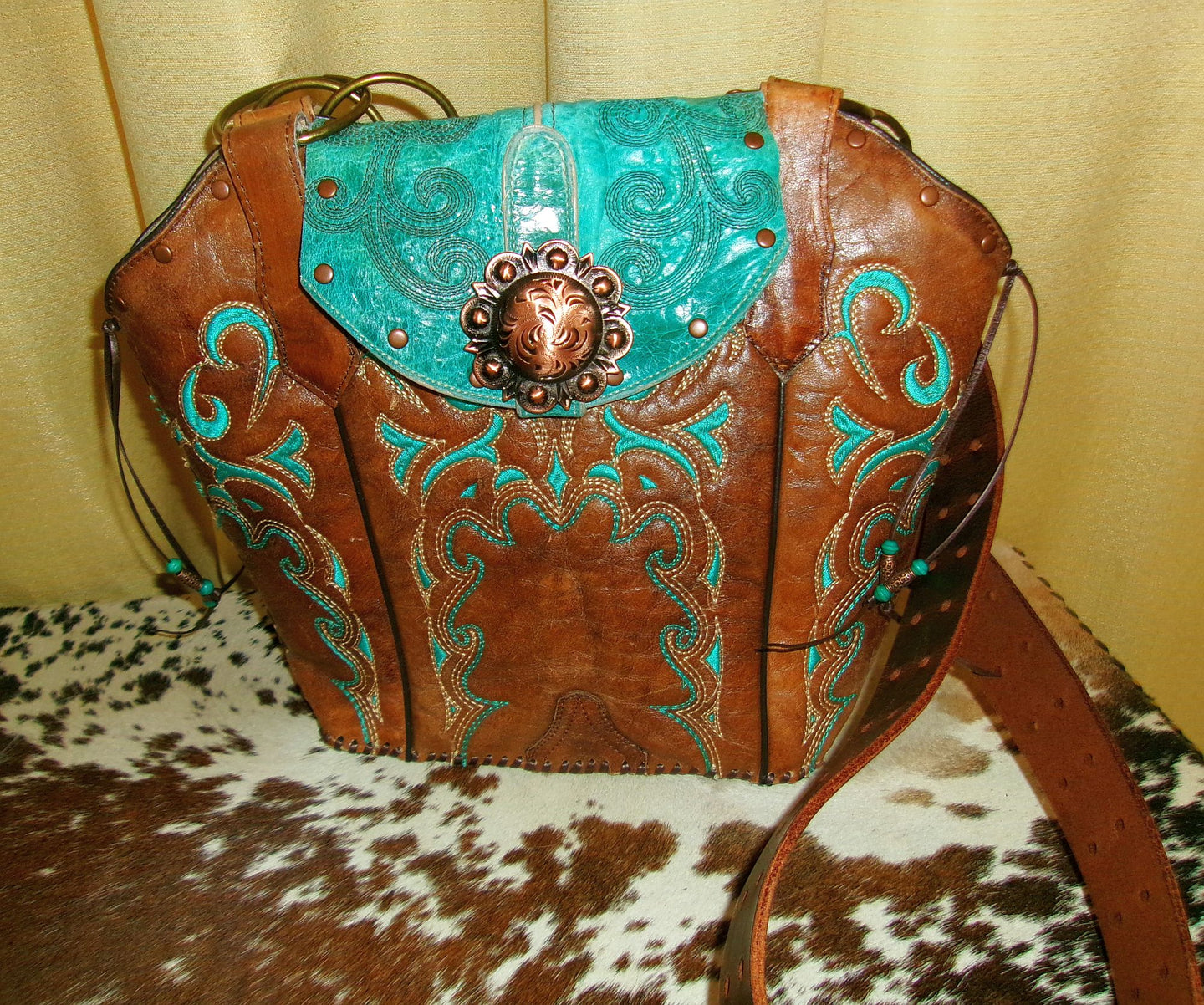 Brown leather handbag with turquoise accents and decorative studs on a cowhide surface.