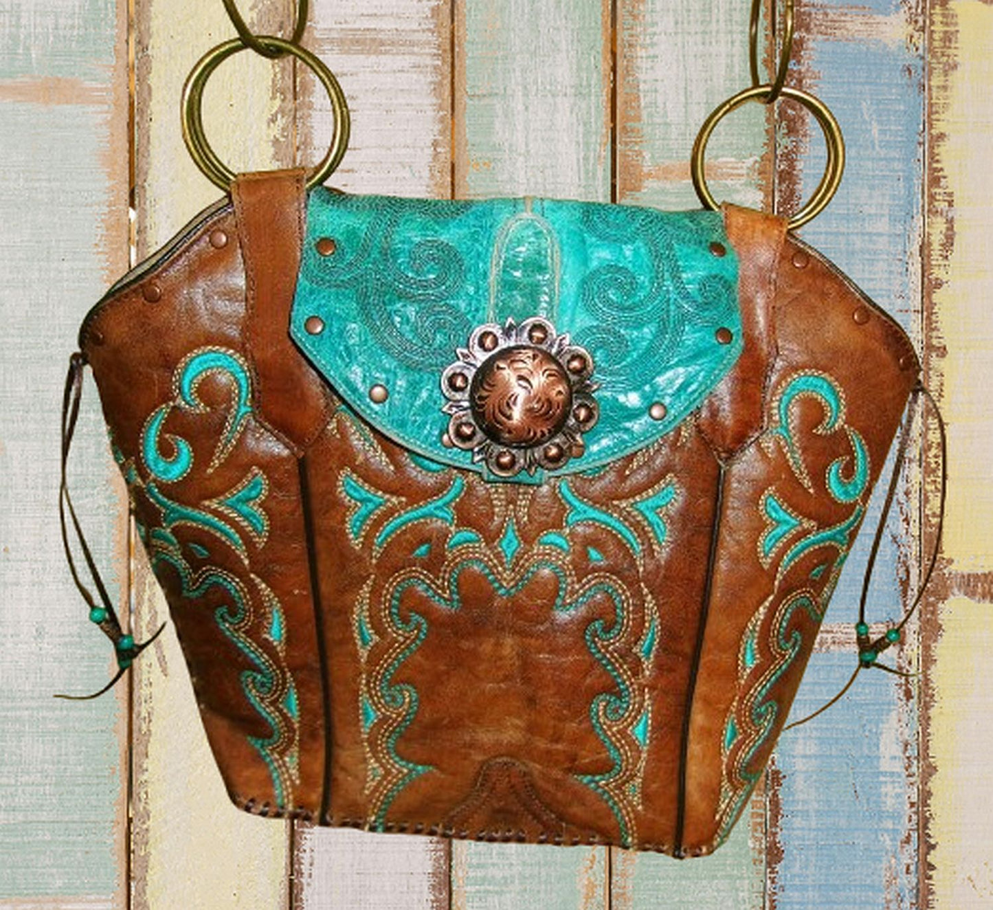 Brown leather handbag with turquoise accents and decorative studs on a wooden surface.