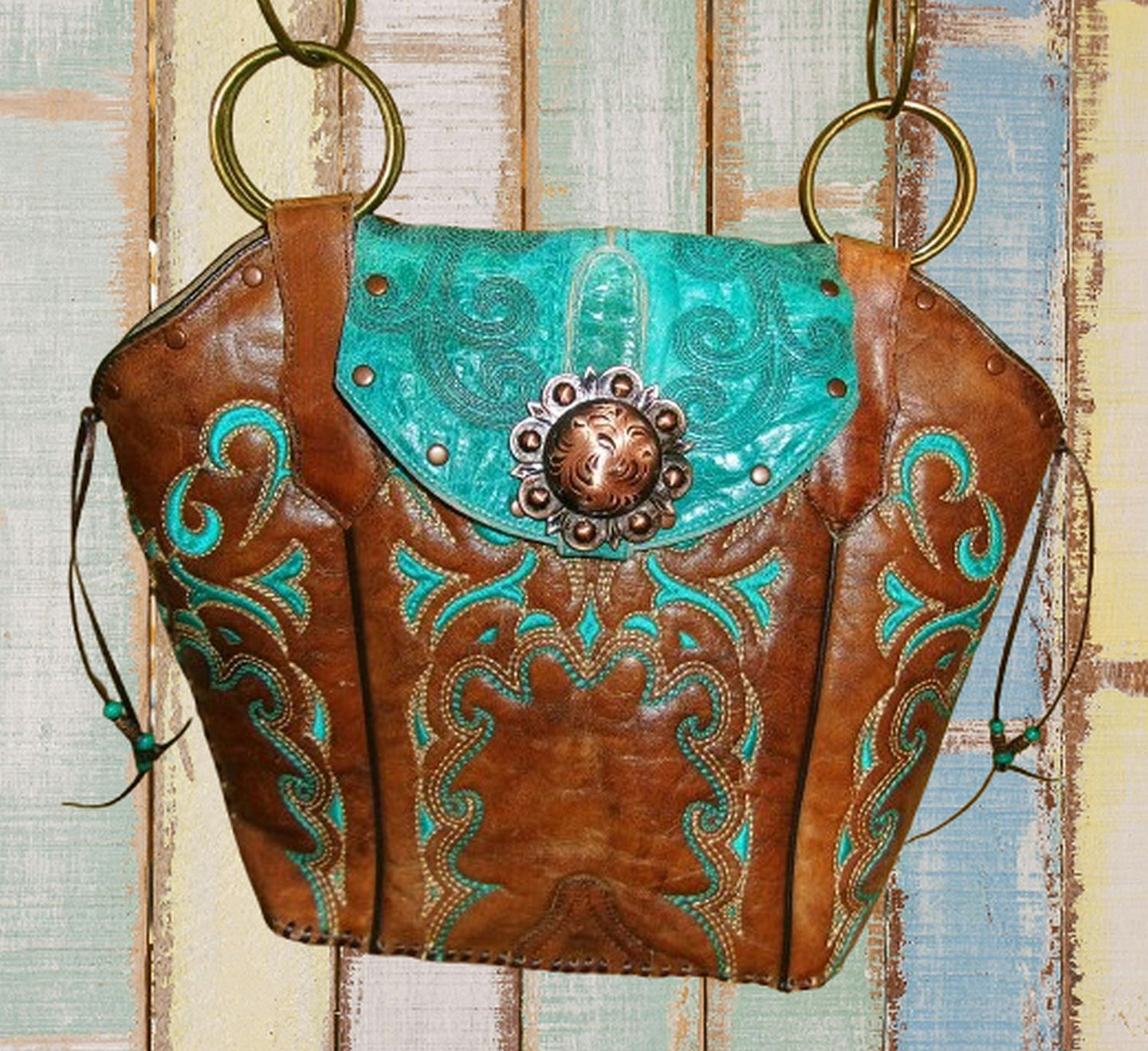 Brown leather handbag with turquoise accents and decorative studs on a wooden surface.