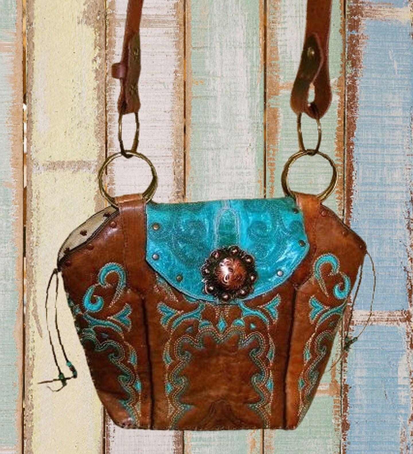 Brown leather handbag with turquoise accents and decorative elements on a wooden background