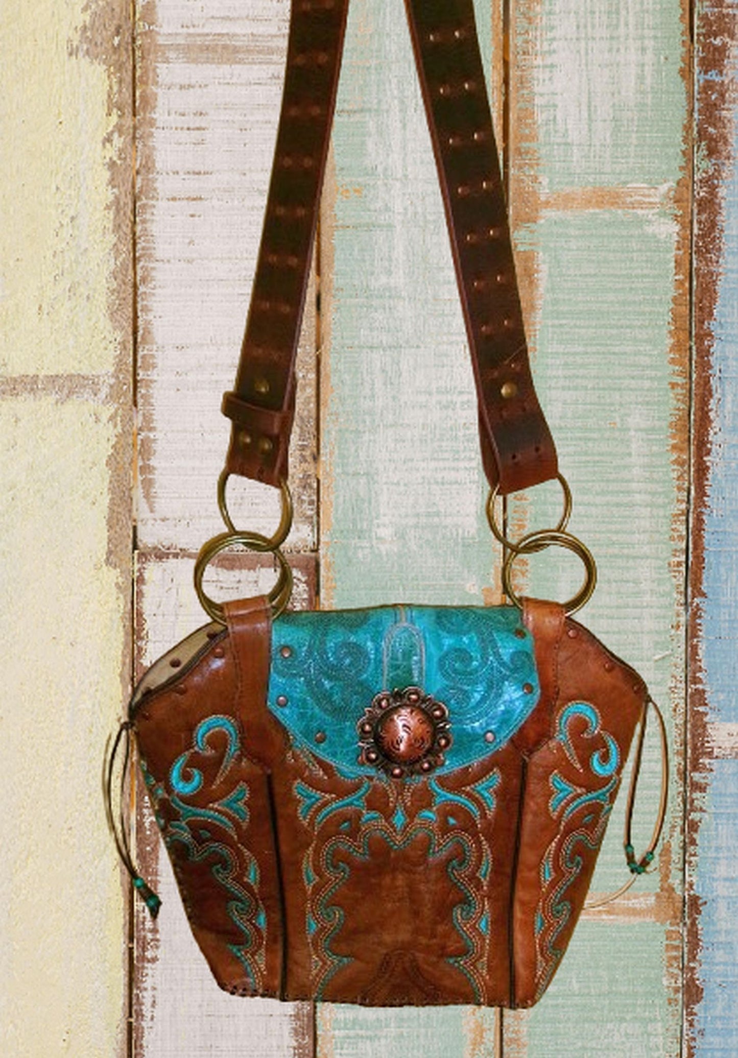 Brown leather handbag with turquoise accents and decorative elements on a wooden background