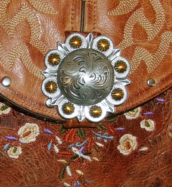 Close-up of a decorative leather bag with floral embroidery and a metallic concho.