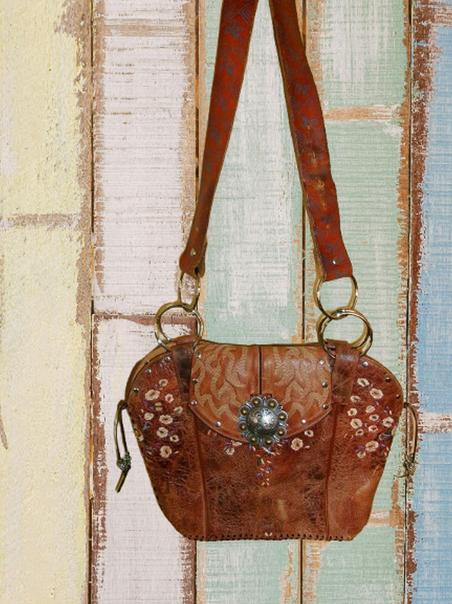 Brown leather handbag with floral patterns and decorative clasp on a wooden surface
