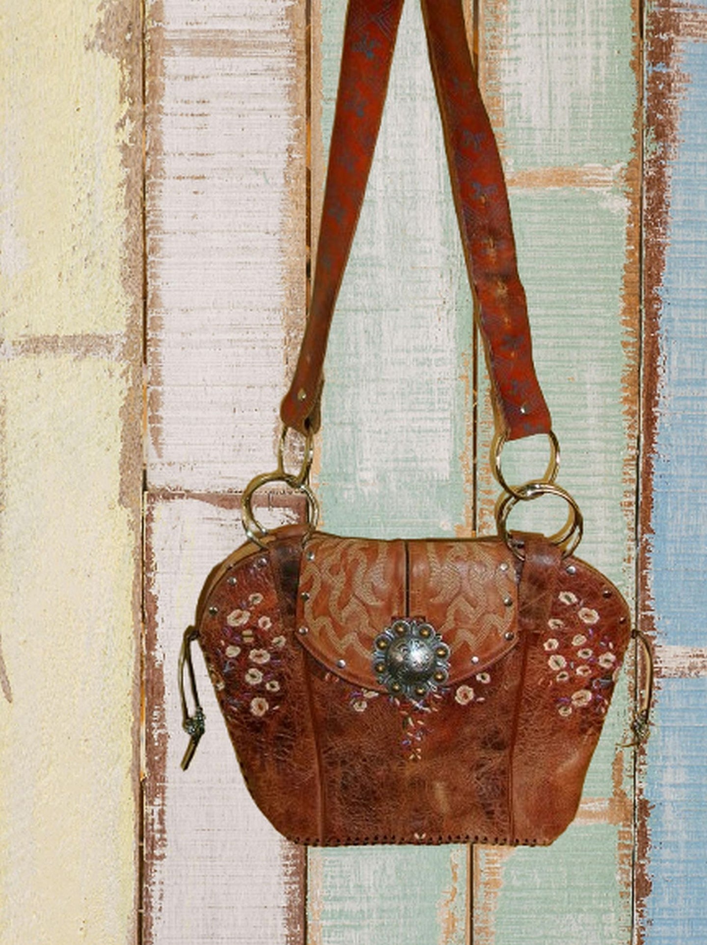 Brown leather handbag with floral patterns and decorative clasp on a wooden surface