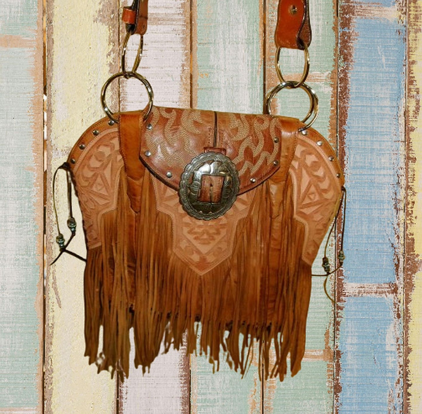 Brown leather handbag with fringe and a decorative buckle on a textured background