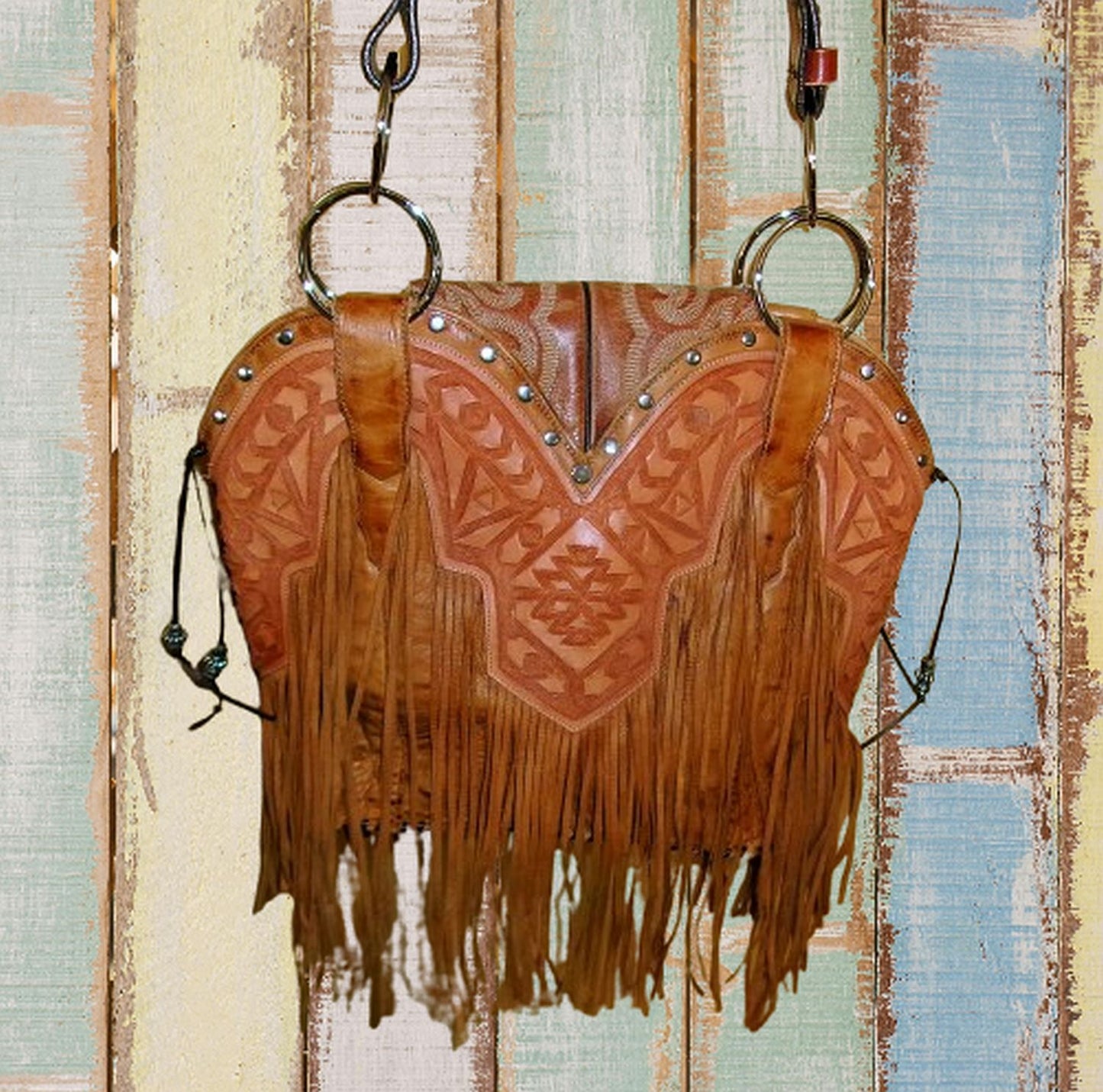 Brown leather bag with fringe and embossed design on a textured wooden background