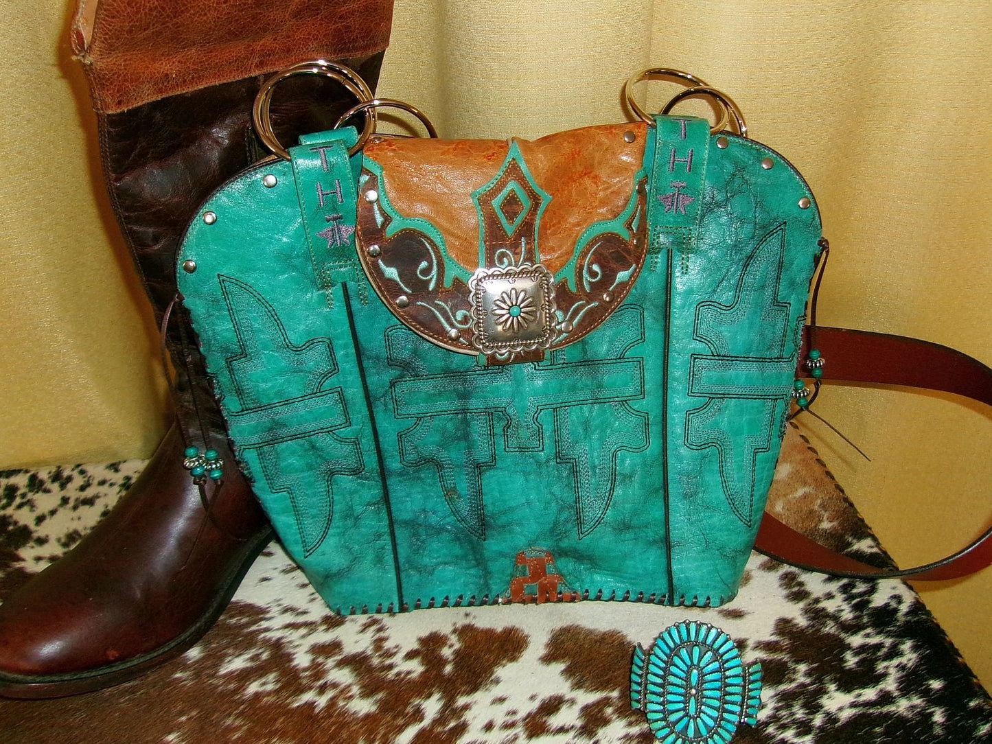 Turquoise handbag with brown accents and a boot on a patterned surface