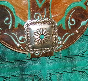 Close-up of a decorative belt buckle with turquoise stone on teal leather background