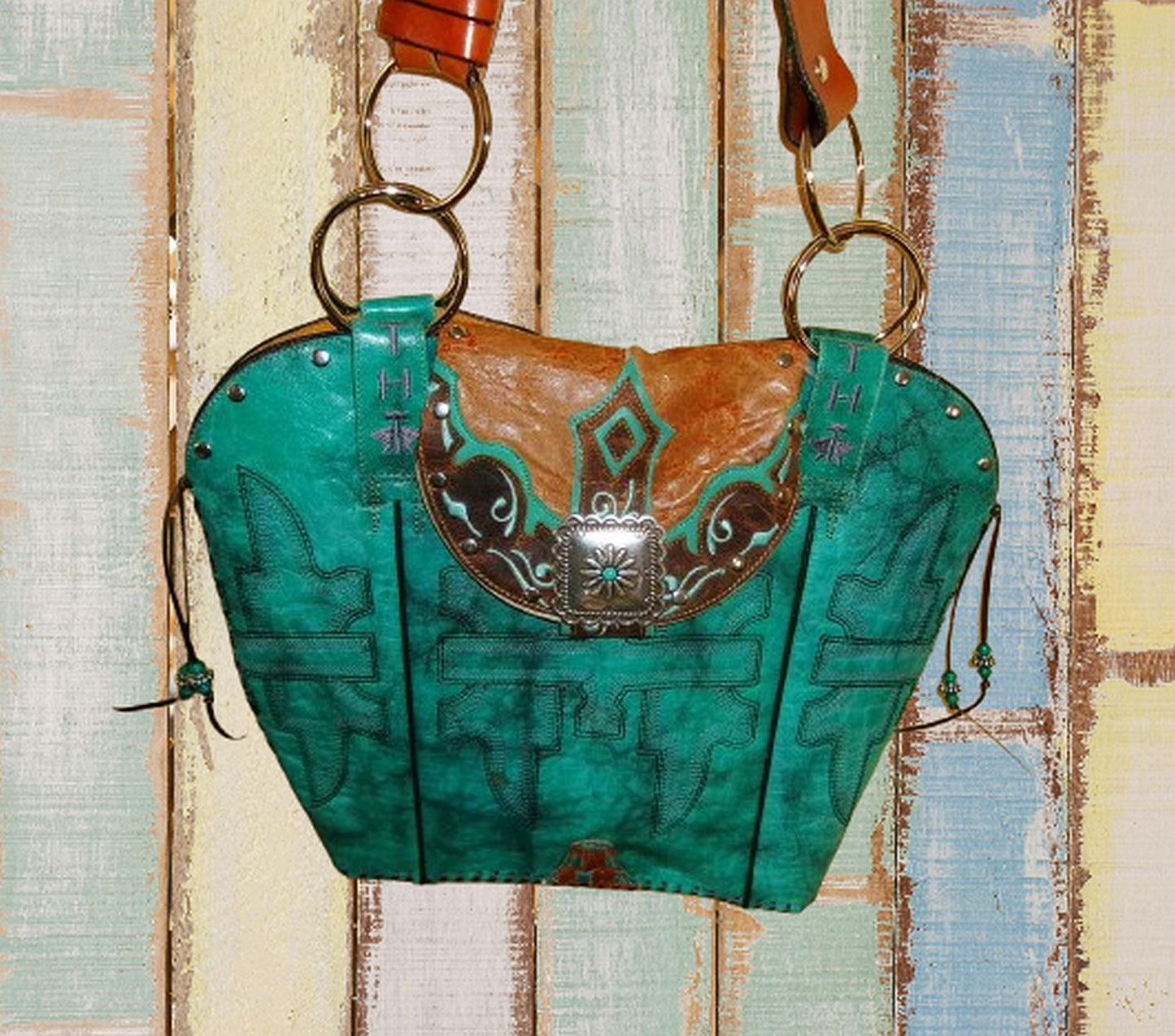 Turquoise leather handbag with brown accents on a wooden surface