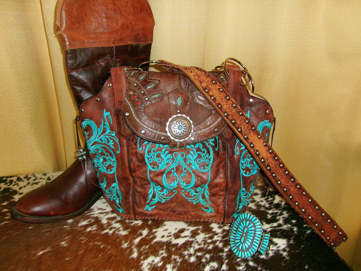 Brown leather handbag with turquoise designs and a matching boot on a patterned surface.