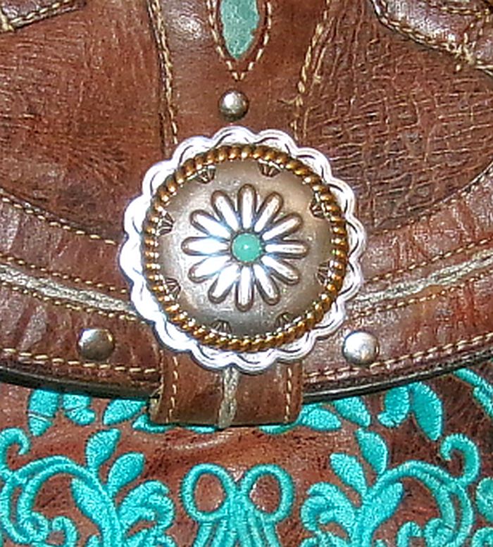 Close-up of a brown leather boot with decorative metal concho and turquoise embroidery.