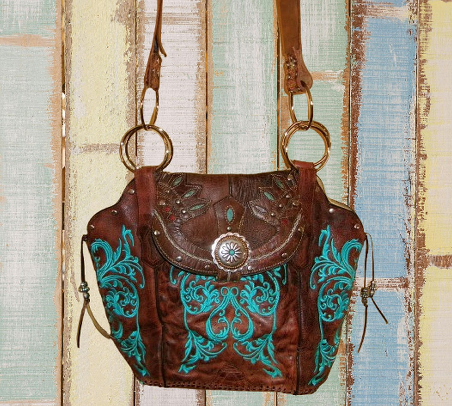 Brown leather handbag with turquoise patterns on a textured wooden background