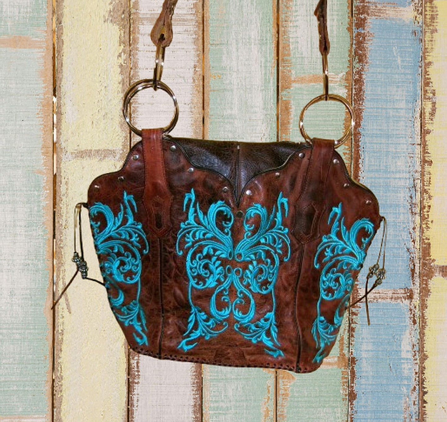 Brown leather bag with blue embroidery against a rustic wooden background
