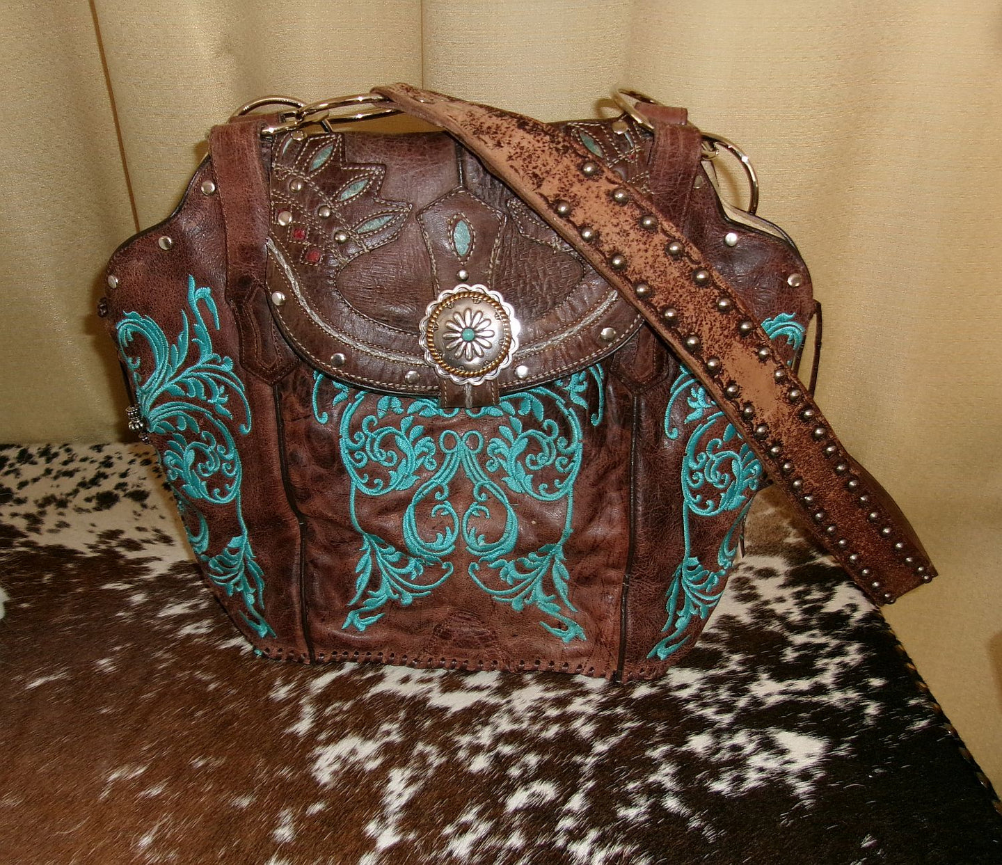 Brown leather handbag with turquoise embroidery on a cowhide surface