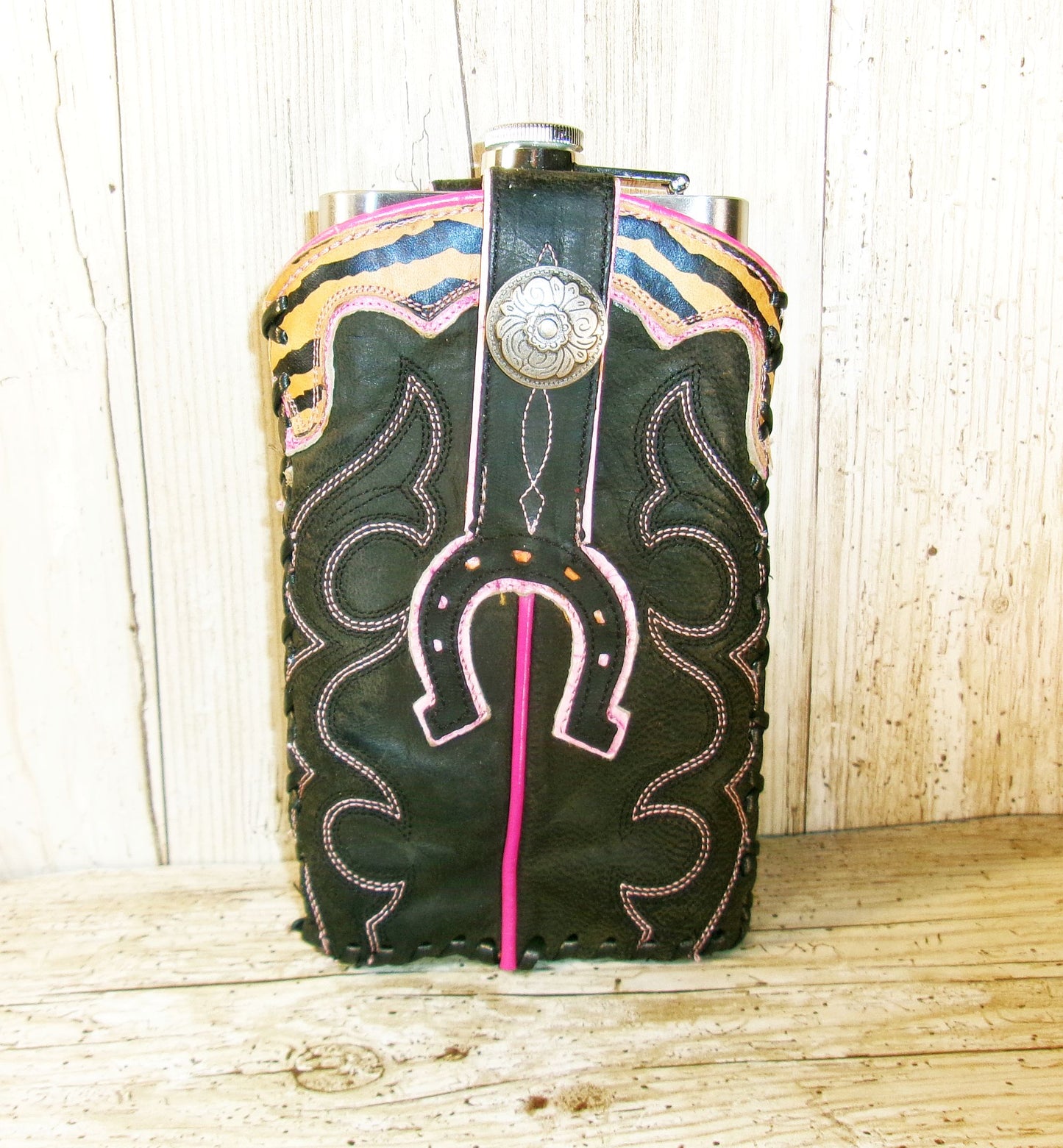 Flask with black leather wrap and pink stitching on a wooden surface