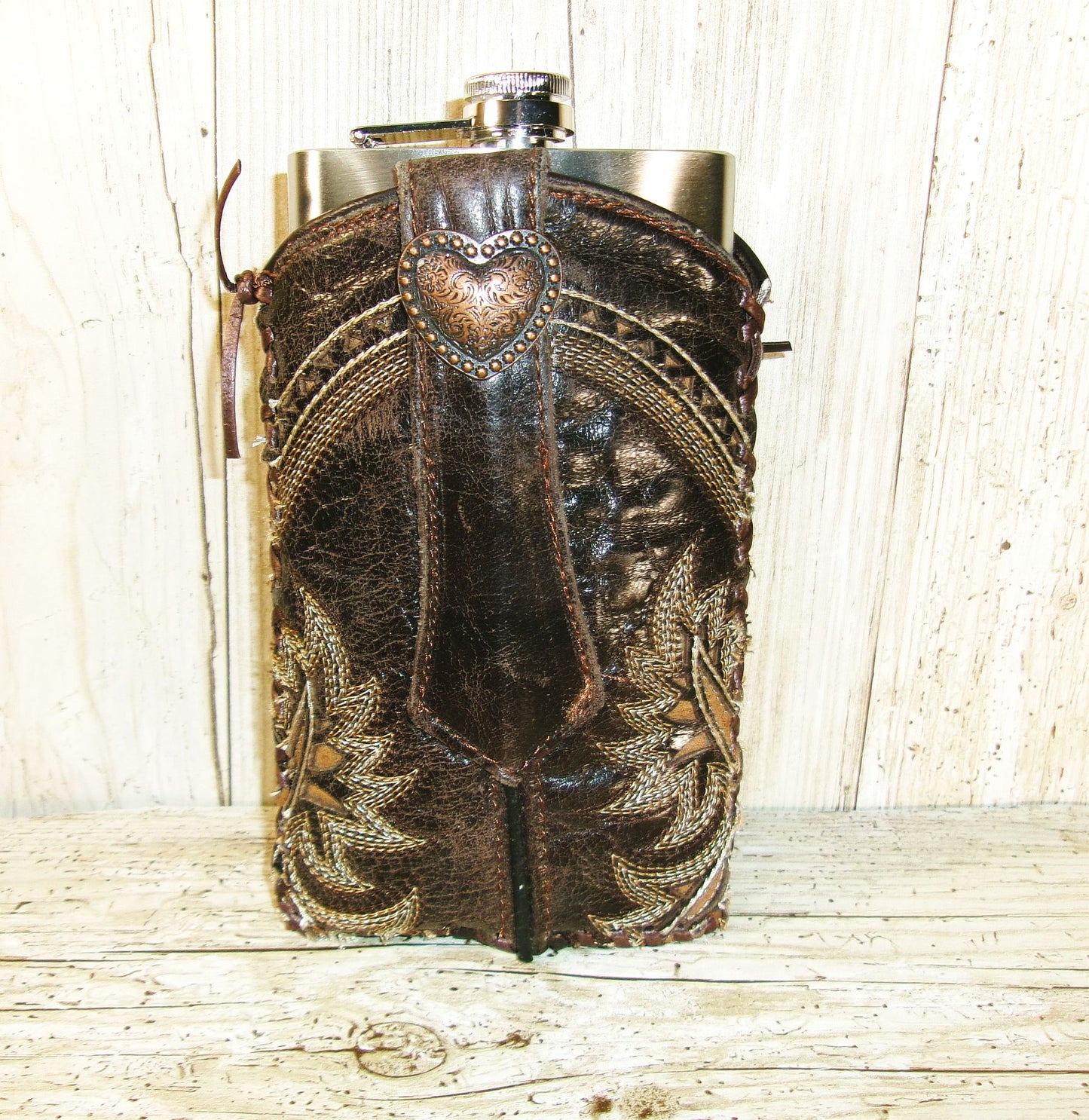 Decorative hip flask with leather cover and heart emblem on a wooden surface