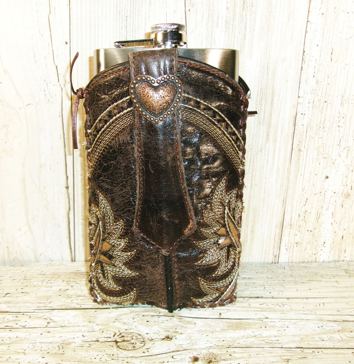 Decorative hip flask with leather cover and heart emblem on a wooden surface