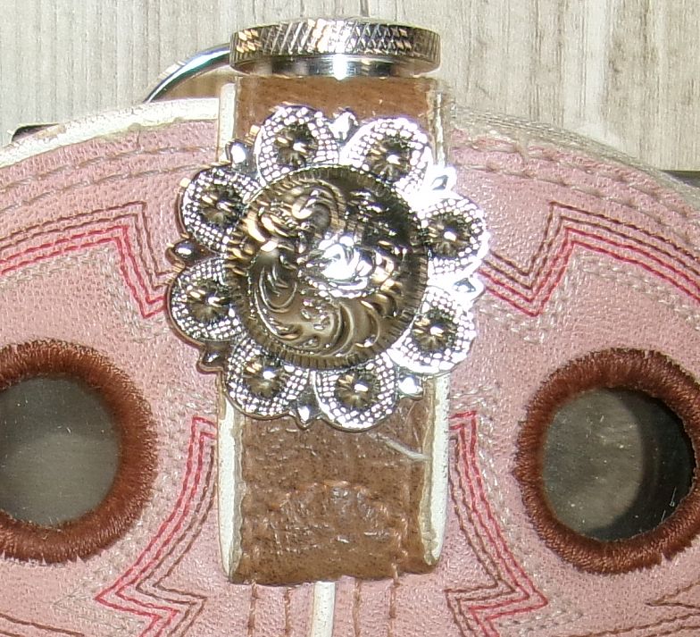 Close-up of a decorative leather buckle with intricate metalwork on a pink and brown background.
