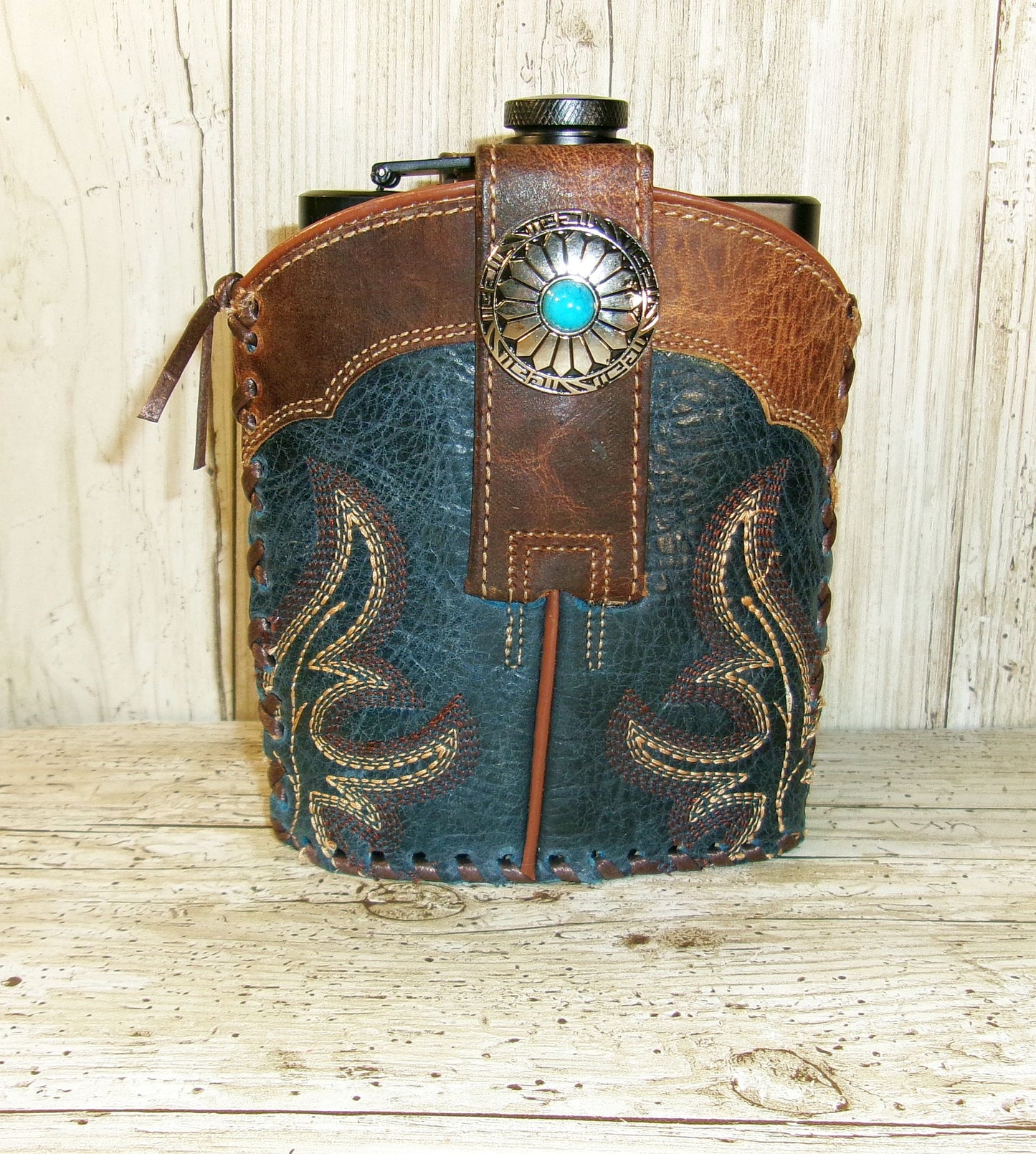 Leather and denim pouch with decorative stitching and turquoise stone on a wooden surface