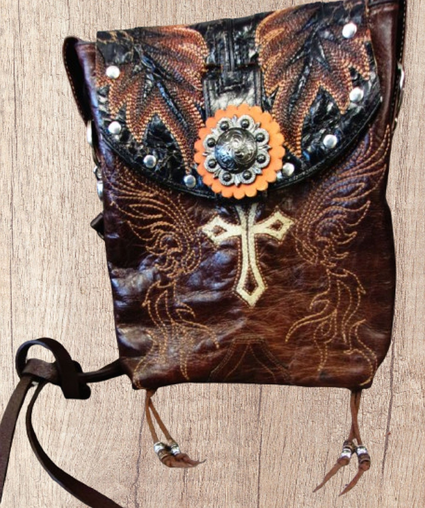 Decorative leather bag with cross design and embellishments on a wooden surface
