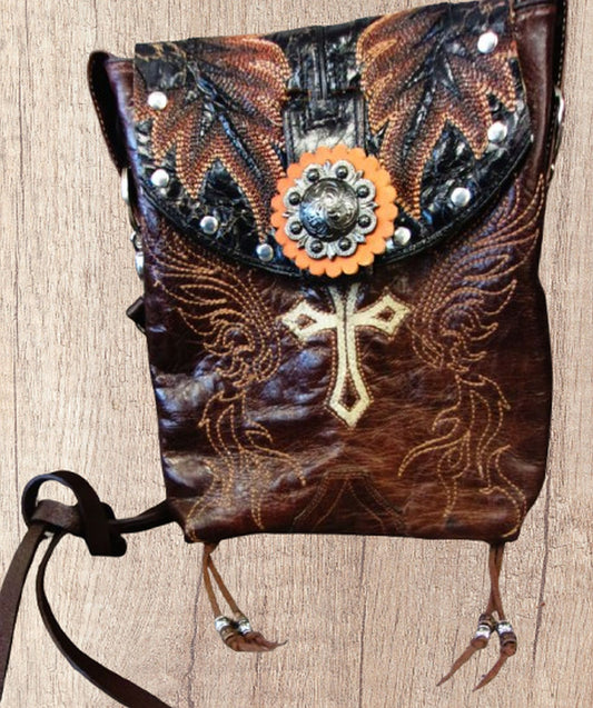 Decorative leather bag with cross design and embellishments on a wooden surface