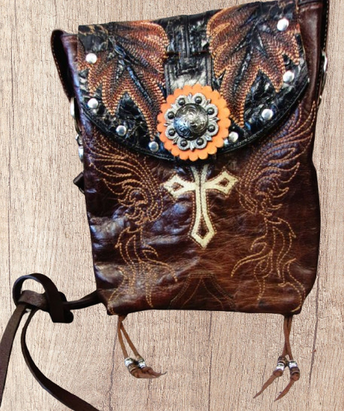 Decorative leather bag with cross design and embellishments on a wooden surface
